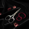 Silver embroidery scissors with engraved plum blossom handle on black velvet with dried petals