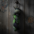 Hex hand-dyed sock yarn hanging from iron hook against weathered barn wood with painted hex signs
