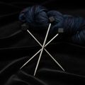 Black hexagonal silicone needle tip protectors on dark knitting needles against black velvet
