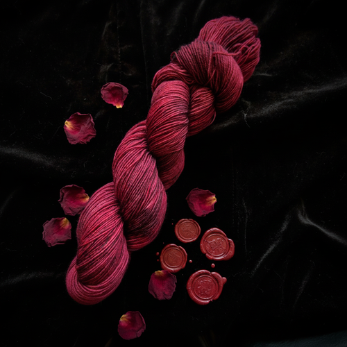Blood Petal hand-dyed yarn in magenta-crimson on black velvet with dried rose petals