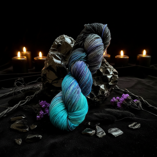 Depths hand-dyed yarn draped over obsidian crystals with candle bokeh — teal to near-black fade